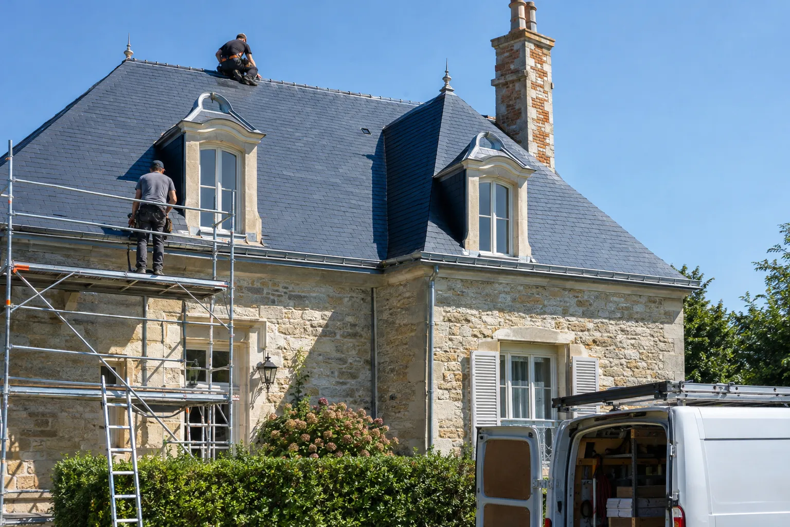 Un toit d’ardoise neuf terminé sur une maison bourgeoise en pierre, sous un ciel bleu.